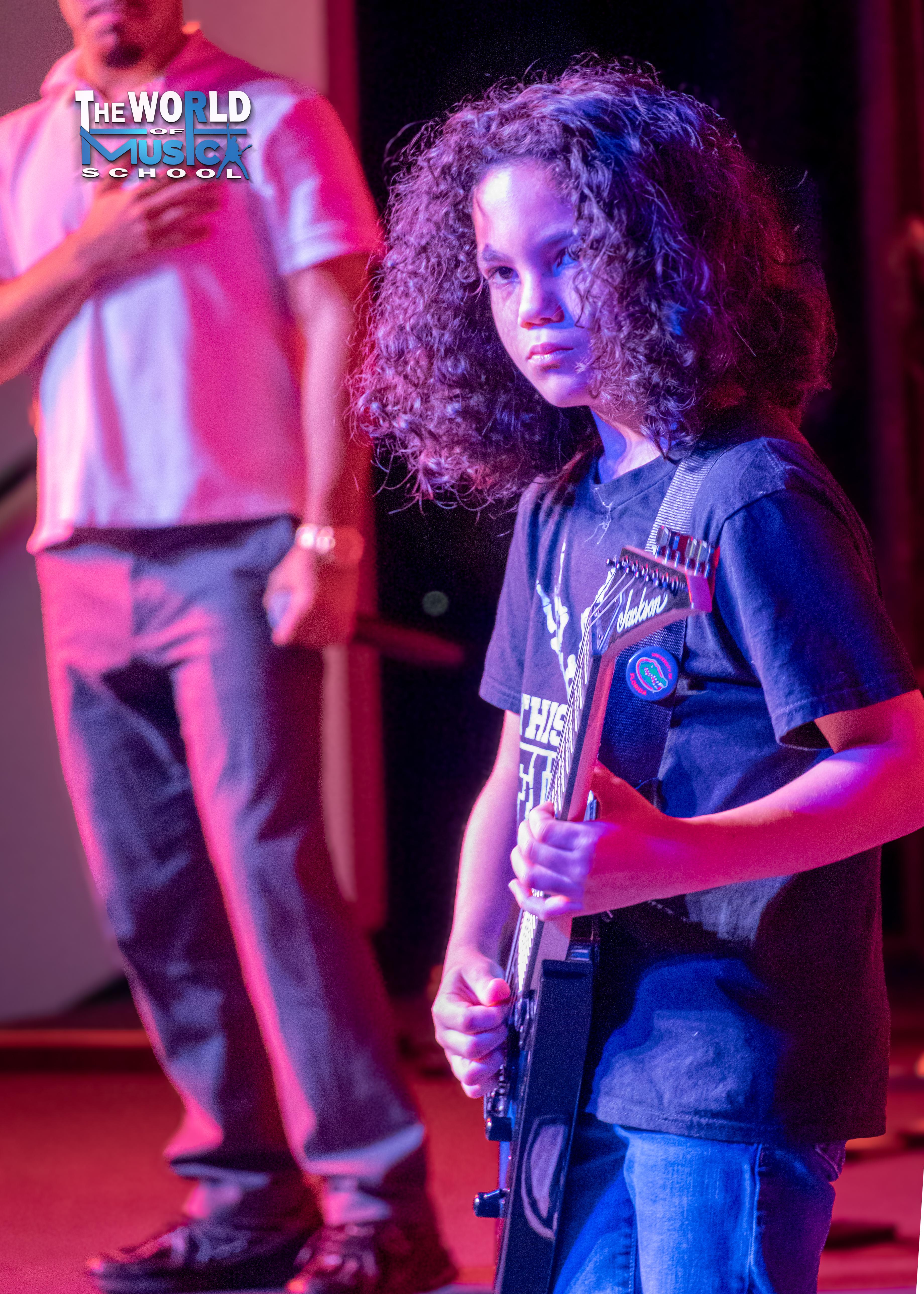 Young girl performing guitar on stage with purple lighting