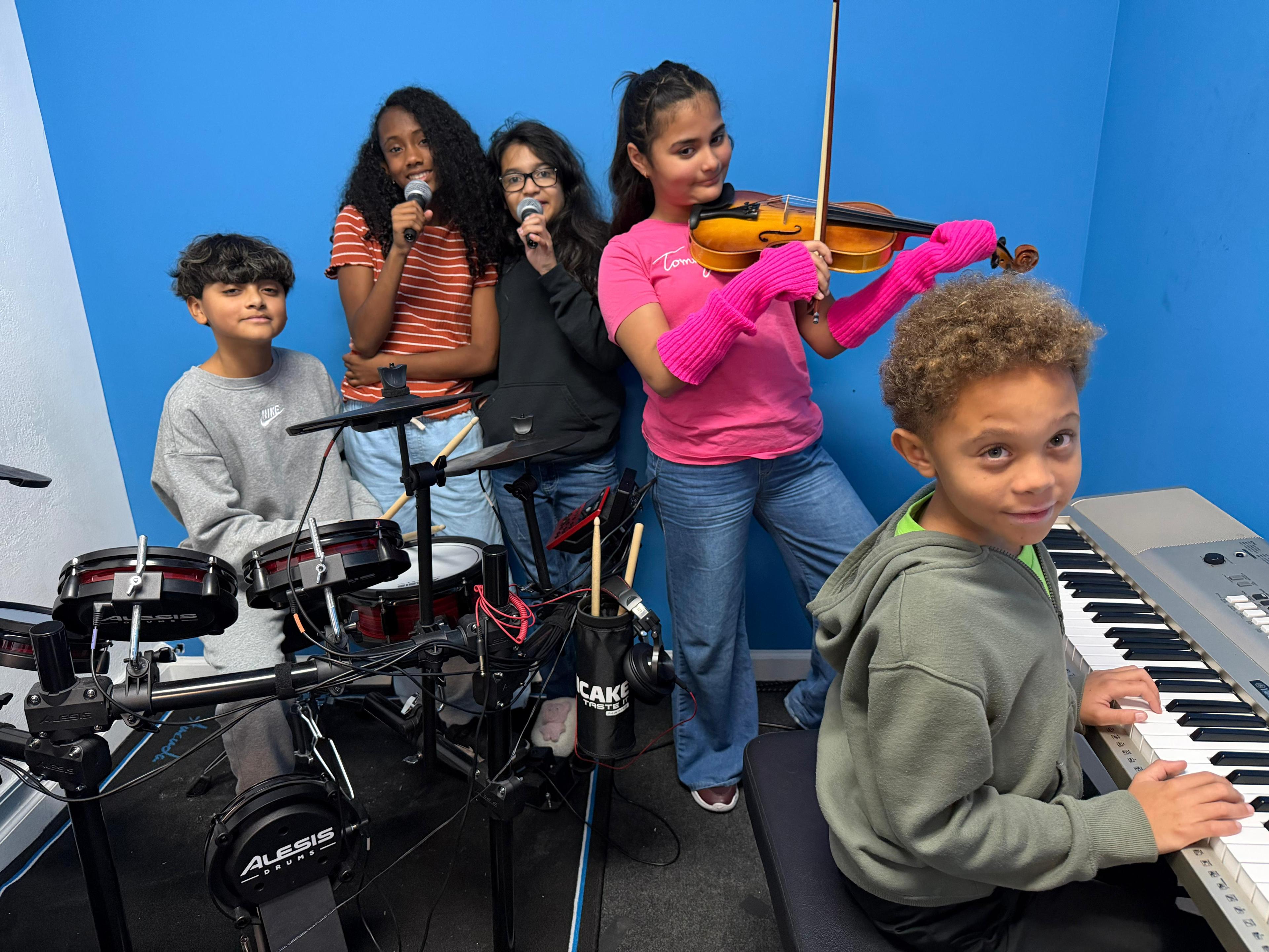Kids playing violin, drums, piano and singing together in classroom